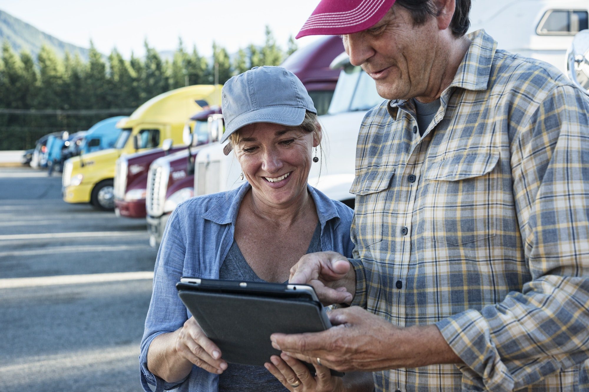 Happy woman and man truck driving team working on their driving log in a truck stop parking lot.